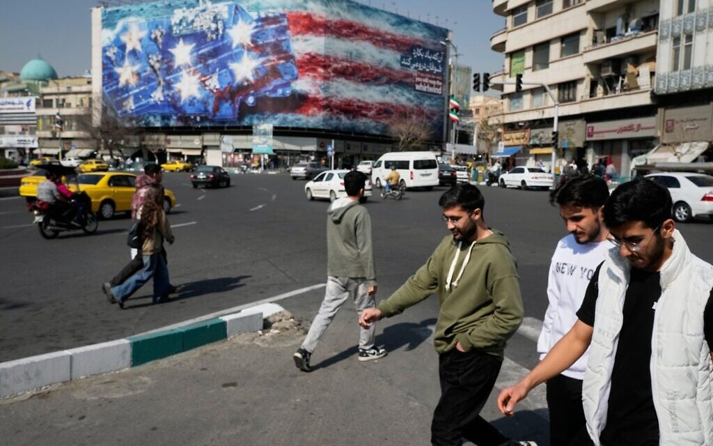 Pedestrians walk past a billboard depicting a US aircraft carrier with damaged fighter jets on its deck and a sign in Farsi and English reading, "If you sow the wind, you'll reap the whirlwind," at Enqelab-e-Eslami (Islamic Revolution) Square in Tehran, Iran, Sunday, Feb. 22, 2026. (AP Photo/Vahid Salemi)