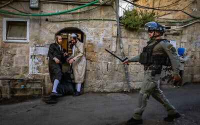 A Border Police officer walks past a Haredi Jew in Mea Shearim, Jerusalem on April 15, 2025. (Chaim Goldberg/Flash90)