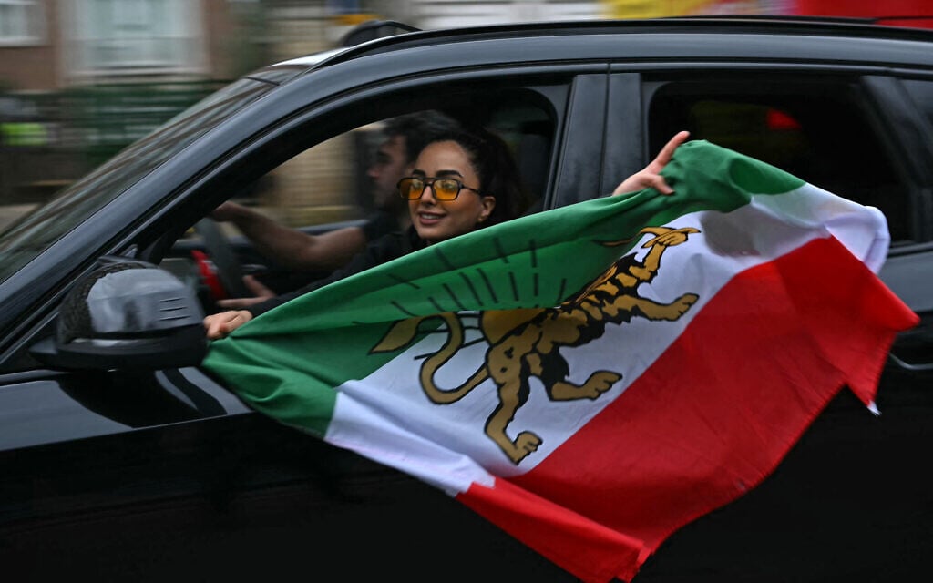 A woman waves a pre-1979 revolution Iranian flag with the Lion and Sun emblem, from a car window during a drive-by celebration outside the Iranian Embassy in central London, on March 1, 2026. (JUSTIN TALLIS / AFP)
