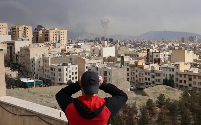 A man looks through biculars as a plume of smoke rises after a military strike on the capital Tehran on March 2, 2026.  (Photo by ATTA KENARE / AFP)