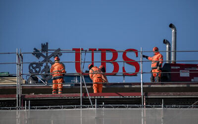 Workers operates next to a sign of Swiss banking giant UBS on the top of a building in Zurich, on March 4, 2026. (Fabrice COFFRINI / AFP)
