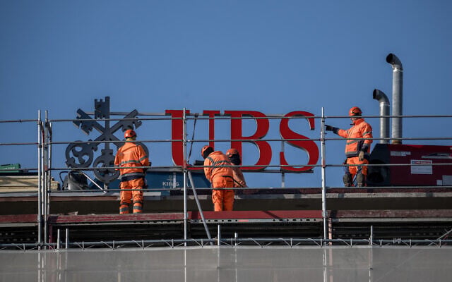 Workers operates next to a sign of Swiss banking giant UBS on the top of a building in Zurich, on March 4, 2026. (Fabrice COFFRINI / AFP) Workers operates next to a sign of Swiss banking giant UBS on the top of a building in Zurich, on March 4, 2026. (Fabrice COFFRINI / AFP)
