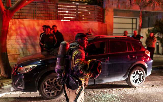 A firefighter holds a helmet as he operates outside a building hit by a projectile in a city in outskirts of Tel Aviv on March 6, 2026. (ILIA YEFIMOVICH / AFP)