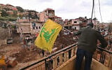 This photograph taken during a media tour organized by Hezbollah shows a man installing a flag of Hezbollah on the balcony of a damaged building at Nabi Chit town after an Israeli military operation in the Bekaa Valley of Lebanon, on March 7, 2026. (Photo by FADEL itani / AFP)