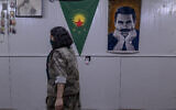 A female Kurdish fighter from the Iranian Kurdish armed faction Kurdistan Free Life Party (PJAK) passes a poster of Abdullah Ocalan, the jailed founder of the Kurdistan Workers' Party (PKK), at a site near the Iraqi border with Iran in Iraq's autonomous Kurdistan region, on March 8, 2026. (Photo by AFP)