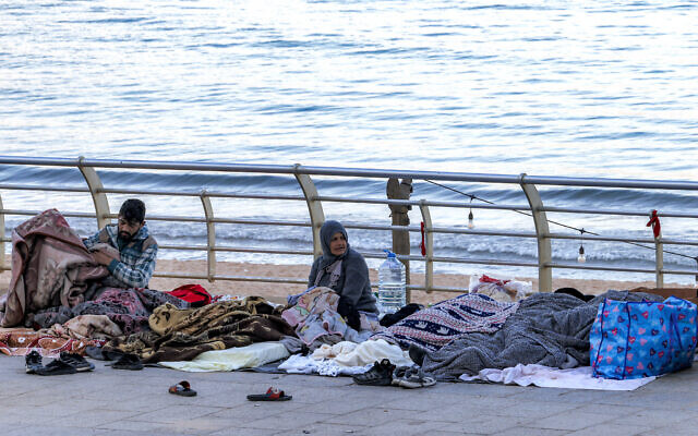 A woman looks on as people sleep wrapped in blankets in a makeshift encampment along the waterfront in Beirut on March 10, 2026, as civilians who fled the city's southern suburbs due to the Israel-Hezbollah conflict remain displaced. (Anwar AMRO / AFP) A woman looks on as people sleep wrapped in blankets in a makeshift encampment along the waterfront in Beirut on March 10, 2026, as civilians who fled the city's southern suburbs due to the Israel-Hezbollah conflict remain displaced. (Anwar AMRO / AFP)