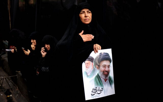 An Iranian woman holds a poster bearing the portraits of Iran's slain supreme leader Ali Khamenei (L) and of his son, the country's new Supreme Leader Mojtaba Khamenei, during the funerals of Iran's Revolutionary Guards Corps (IRGC) commanders, army commanders and others killed in the early days of the United States and Israeli strikes on Iran, at Enghelab Square in Tehran on March 11, 2026. (ATTA KENARE / AFP)