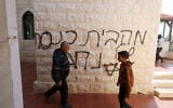 Palestinians walk past Hebrew graffiti made by extremist settlers on the wall of the Mohammad Fayyad mosque in the Palestinian village of Duma, south of Nablus in the northern West Bank, on March 12, 2026. (JAAFAR ASHTIYEH / AFP)