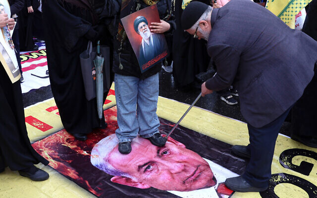 An Iranian man pokes his crutch at an image of Prime Minister Benjamin Netanyahu, as others stand on the poster in the Al-Quds Day rally, in Tehran on March 13, 2026 (AFP)