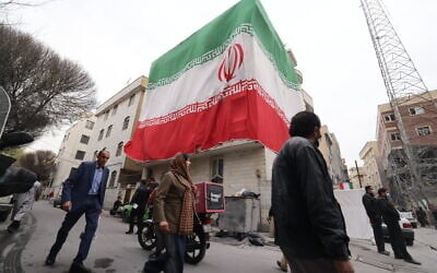 A huge Iranian flag adorns a building as Iranians walk past damaged structures following an earlier military strike in the Iranian capital, Tehran, on March 15, 2026. (Atta KENARE / AFP) /