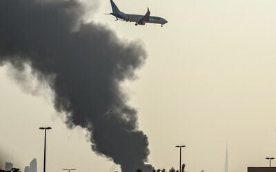 A FlyDubai aircraft prepares to land as a smoke plume rises from an active fire near Dubai International Airport in Dubai on March 16, 2026. (AFP)
