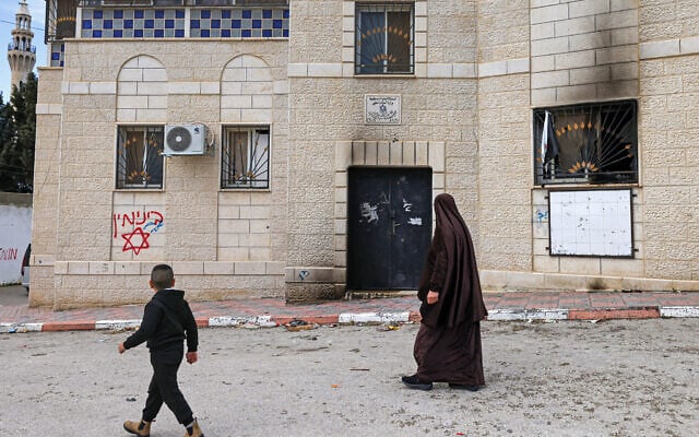 A Palestinian woman and boy walk past Hebrew graffiti (reading: "Binyamin") on the walls of a damaged house following a reported attack by extremist settlers in Jalud village, south of Nablus in the West Bank, on March 22, 2026. (JAAFAR ASHTIYEH / AFP) A Palestinian woman and boy walk past Hebrew graffiti (reading: "Binyamin") on the walls of a damaged house following a reported attack by extremist settlers in Jalud village, south of Nablus in the West Bank, on March 22, 2026. (JAAFAR ASHTIYEH / AFP)
