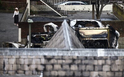 A woman walks next to damaged and burnt out ambulances (R) in the Golders Green area of north London on March 23, 2026, after volunteer ambulances run by a Jewish organization were set on fire overnight. (Photo by Henry NICHOLLS / AFP)