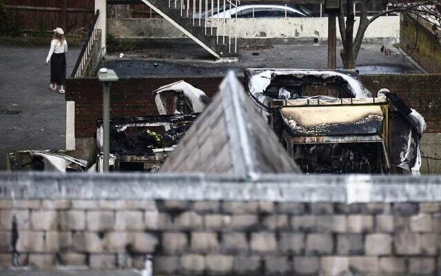 A woman walks next to damaged and burnt out ambulances (R) in the Golders Green area of north London on March 23, 2026, after volunteer ambulances run by a Jewish organization were set on fire overnight. (Photo by Henry NICHOLLS / AFP)