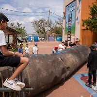 Children play with an Iranian missile remnant that fell in a school courtyard in the Israeli settlement of Peduel, in the West Bank on March 23, 2026. (Maya Levin / AFP) /