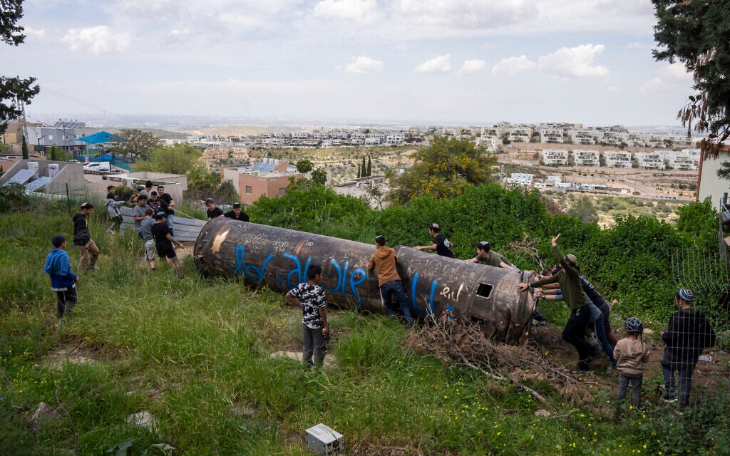 Children move a part of an Iranian missile remnant that fell in a school courtyard in the Israeli settlement of Peduel, West Bank on March 23, 2026. (Maya Levin / AFP) /