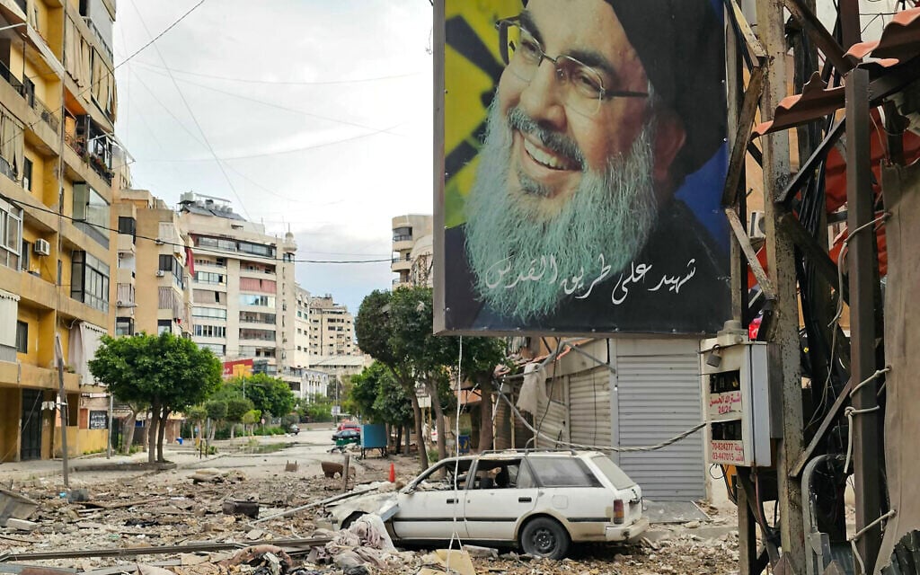 A banner bearing the image of Hassan Nasrallah, the slain Hezbollah leader hangs from a building along a street littered with building debris at the site of an overnight Israeli airstrike that targeted a neighborhood in Beirut's southern suburbs on March 25, 2026.  (Photo by AFP)