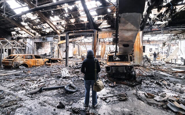 Journalists stand next to the wreckage of vehicles during the visit of a car service centre in eastern Tehran that was apparently hit by a missile strike, on March 28, 2026.(ATTA KENARE / AFP) /