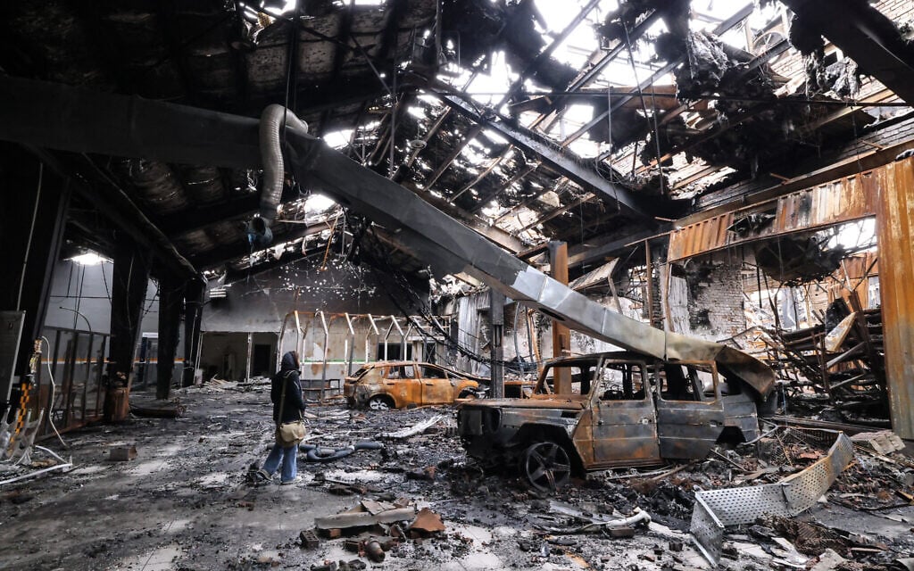 A journalist stands next to the wreckage of a vehicle at car service center in eastern Tehran, Iran, that was hit by a missile strike, on March 28, 2026. (ATTA KENARE / AFP) /