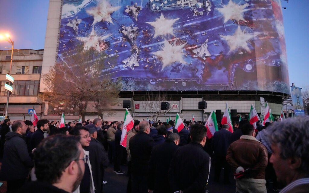 Government supporters gather in mourning after state TV officially announced the death of Iranian Supreme Leader Ayatollah Ali Khamenei, under a billboard with graphic showing a US aircraft carrier with damaged fighter jets on its deck, in Tehran, Iran, Sunday, March 1, 2026. (AP/Vahid Salemi)