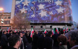 Government supporters gather in mourning after state TV officially announced the death of Iranian Supreme Leader Ayatollah Ali Khamenei, under a billboard with graphic showing a US aircraft carrier with damaged fighter jets on its deck, in Tehran, Iran, Sunday, March 1, 2026. (AP/Vahid Salemi)