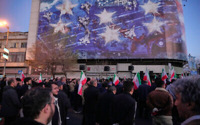 Government supporters gather in mourning after state TV officially announced the death of Iranian Supreme Leader Ayatollah Ali Khamenei, under a billboard with graphic showing a US aircraft carrier with damaged fighter jets on its deck, in Tehran, Iran, Sunday, March 1, 2026. (AP/Vahid Salemi)