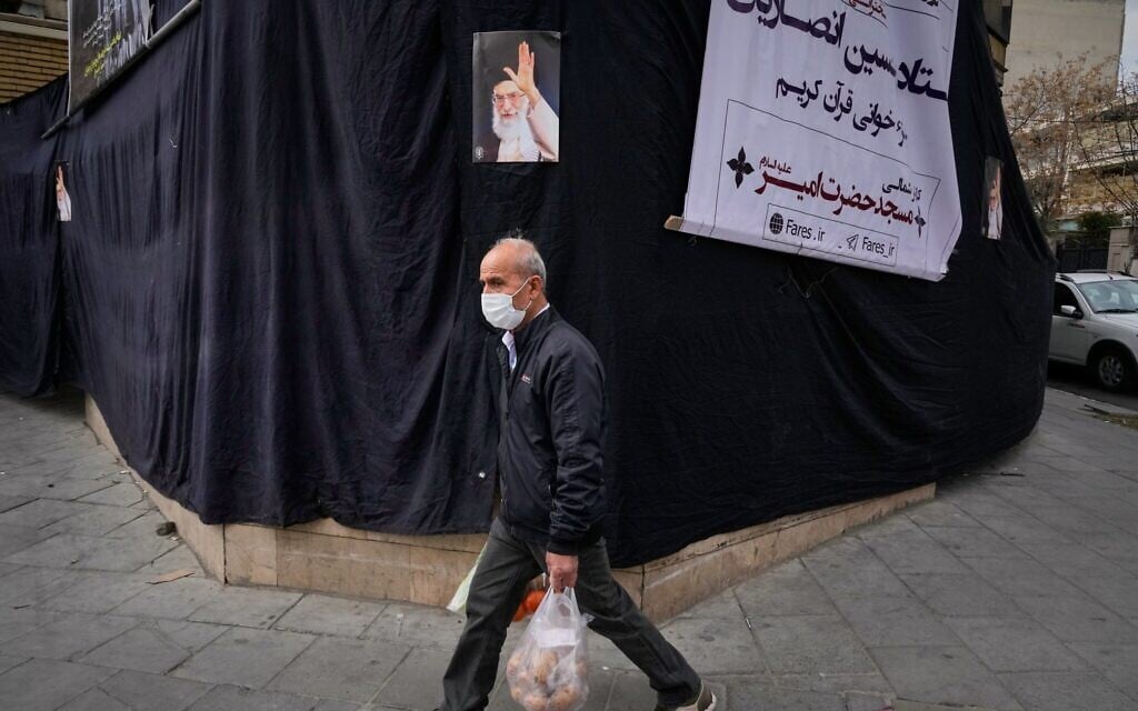 A man carrying groceries walks by a picture of the late Iranian supreme leader Ayatollah Ali Khamenei hanging on a black sheet along the side of a mosque in Tehran, Iran, March 2, 2026. (AP/Vahid Salemi)