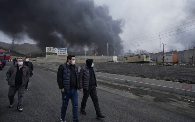 Four men walk as a thick plume of smoke from a US-Israeli strike on an oil storage facility late Saturday lingers in the cloudy sky behind them in Tehran, Iran, Sunday, March 8, 2026. (AP/Vahid Salemi) Four men walk as a thick plume of smoke from a US-Israeli strike on an oil storage facility late Saturday lingers in the cloudy sky behind them in Tehran, Iran, Sunday, March 8, 2026. (AP/Vahid Salemi)