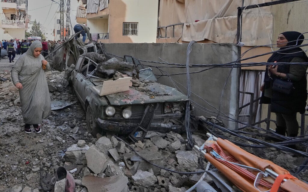 A woman walks past a damaged car at the site of an Israeli airstrike that hit an apartment in the southern port city of Sidon, Lebanon, March 13, 2026. (AP Photo/Mohammed Zaatari) A woman walks past a damaged car at the site of an Israeli airstrike that hit an apartment in the southern port city of Sidon, Lebanon, March 13, 2026. (AP Photo/Mohammed Zaatari)