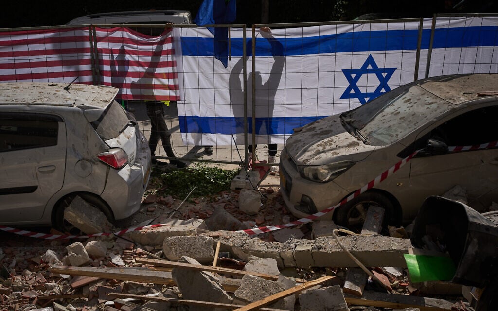 Israeli authorities hang Israeli and US flags at the site struck by an Iranian missile that killed two people, in Ramat Gan, March 18, 2026. (AP Photo/Oded Balilty)