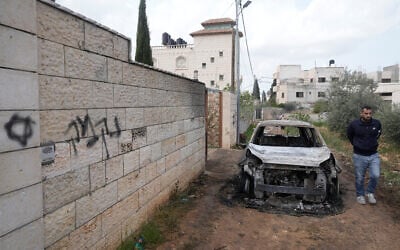 A Palestinian man inspects a torched vehicle next to Hebrew graffiti on a wall that reads "revenge," following a settler rampage through nearby Nablus-area villages, in West Bank village of Deir al-Hatab, March 23, 2026. (AP/Majdi Mohammed) A Palestinian man inspects a torched vehicle next to Hebrew graffiti on a wall that reads "revenge," following a settler rampage through nearby Nablus-area villages, in West Bank village of Deir al-Hatab, March 23, 2026. (AP/Majdi Mohammed)