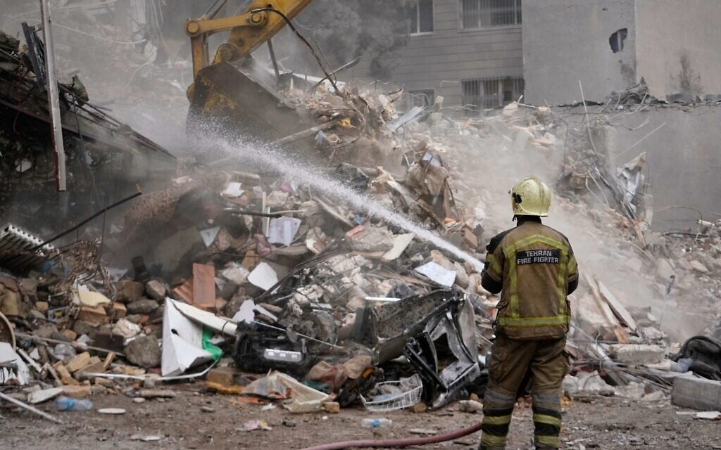 A firefighter hoses down smoldering rubble as a bulldozer clears debris at a residential building hit in an earlier US-Israeli strike in Tehran, Iran, March 23, 2026. (AP Photo/Vahid Salemi)