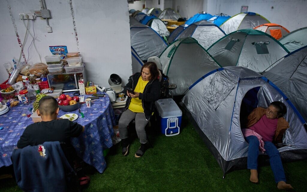 People sit around a makeshift dinner table with groceries beside tents as they take shelter beneath Tel Aviv's central bus station as a precaution against Iranian missile attacks, March 12, 2026. (AP Photo/Oded Balilty)