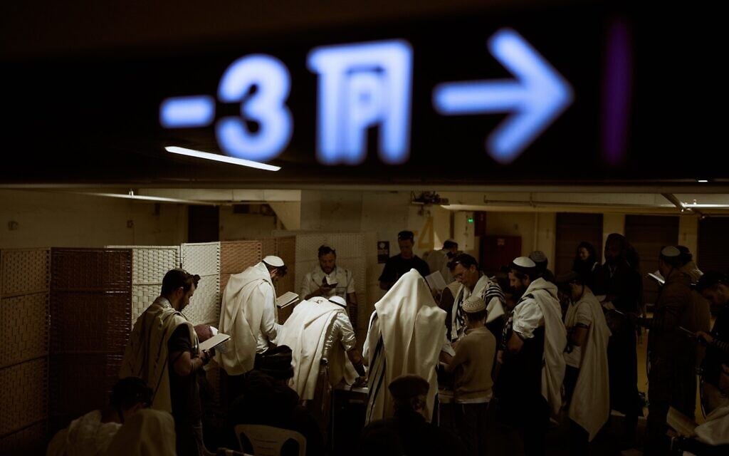 Jewish men wrapped in prayer shawls pray in an underground parking garage used as a shelter against Iranian missile attacks in Tel Aviv, March 3, 2026. (AP Photo/Oded Balilty)
