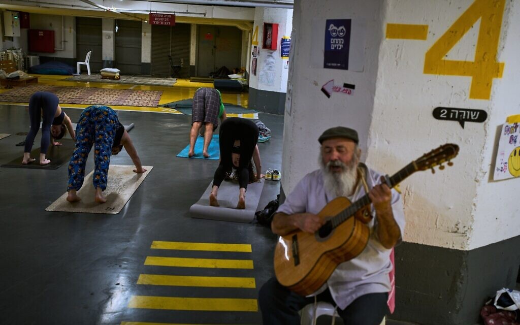 A man plays the guitar as people attend a yoga class in an underground parking garage used as a shelter against Iranian missile attacks in Tel Aviv, March 17, 2026. (AP Photo/Oded Balilty)