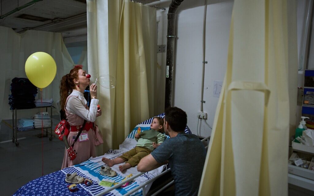 A medical staff member entertains a young patient in a temporary emergency ward set up in a parking garage used as a shelter beneath Sheba Medical Center in Ramat Gan, March 17, 2026. (AP Photo/Oded Balilty)