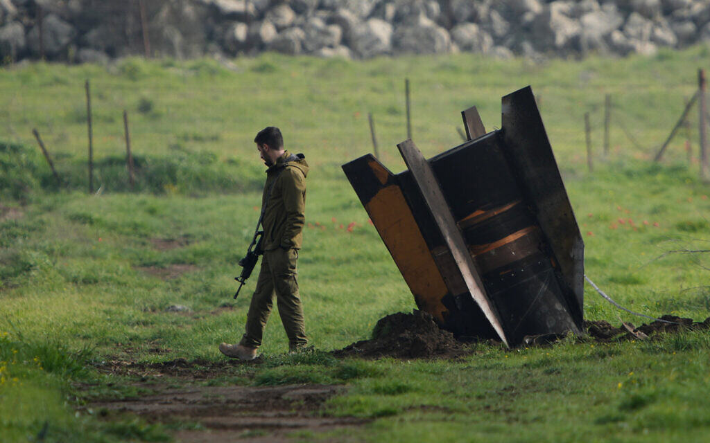 An Israeli soldier stands next to a fragment of a missile fired from Iran and intercepted by Israeli air defense system embedded in an open field in the Golan Heights, March 19, 2026. (AP Photo/Ohad Zwigenberg, File)