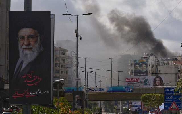 A portrait of Iran's late supreme leader Ayatollah Ali Khamenei, left, is seen, as smoke rises following an Israeli airstrike in Dahiyeh, Beirut's southern suburbs, Lebanon, March 30, 2026. (AP Photo/Hassan Ammar)