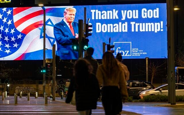 People walk past a sign reading “Thank you God & Donald Trump” in Tel Aviv, March 10, 2026. (Flash90)