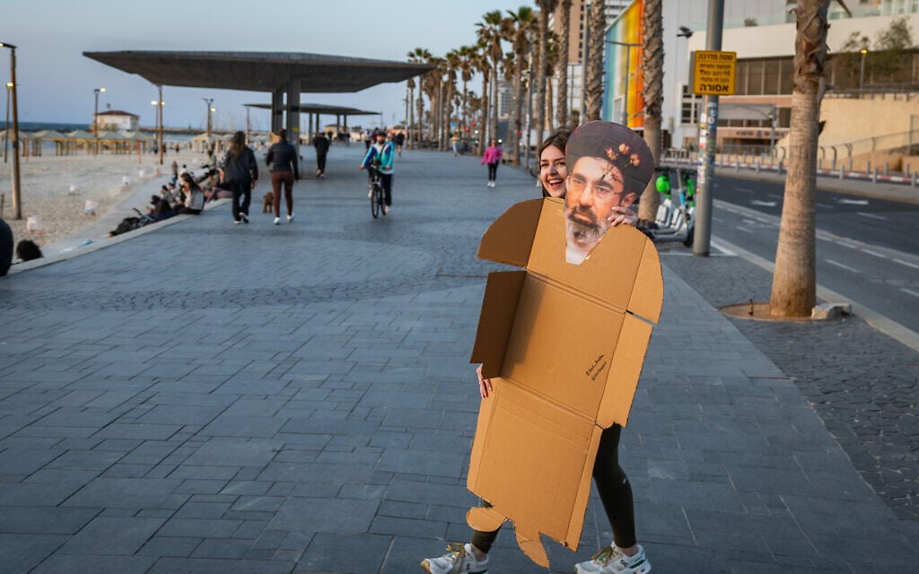 A woman carries a cardboard cutout with the face of Iranian Supreme Leader Mojtaba Khamenei near the beach in Tel Aviv, March 11, 2026. (Chaim Goldberg/Flash90)