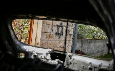 Graffiti is seen through the window of a burnt out car following a settler attack on the village of Deir al-Hatab, east of Nablus in the West Bank, March 23, 2026. (Nasser Ishtayeh/Flash90)