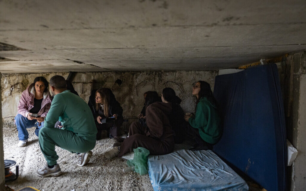 People take cover as a siren warns of incoming missiles at the scene where an Iranian missile hit a home a day earlier, in Moshav Eshtaol, near Beit Shemesh, March 29, 2026. (Chaim Goldberg/Flash90)