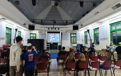 Jerusalem baseball players and their families watch Team Israel play on TV in Jerusalem, March 9, 2026 (Zev Stub/Times of Israel)