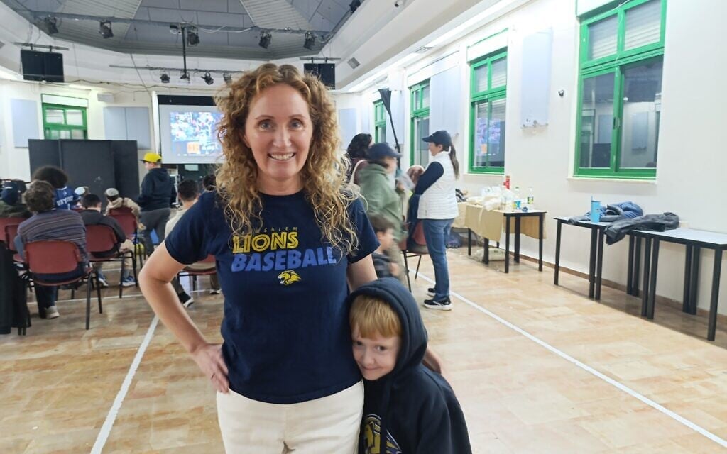 Jerusalem baseball regional director Callie Mitchell and her son watch Team Israel play on TV in Jerusalem, March 9, 2026 (Zev Stub/Times of Israel)