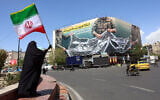 A woman holds the flag of the Islamic Republic of Iran while standing near a billboard that reads, 'The Strait of Hormuz remains closed,' in Tehran, Iran, April 5, 2026. (AFP)