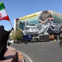 A woman holds the flag of the Islamic Republic of Iran while standing near a billboard that reads, 'The Strait of Hormuz remains closed,' in Tehran, Iran, April 5, 2026. (AFP)