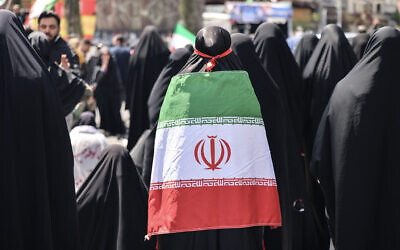 An Iranian woman wrapped in the national flag performs noon prayers as people gather in Tehran's Revolution Square after the United States and Iran agreed to a two-week ceasefire, on April 8, 2026. (ATTA KENARE / AFP) /