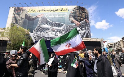 Iranians hold flags of the Islamic Republic of Iran beneath a large billboard reading 'The Strait of Hormuz remains closed,' as people gather in Tehran's Revolution Square after the United States and Iran agreed to a two-week ceasefire, April 8, 2026. (Atta Kenare/AFP)