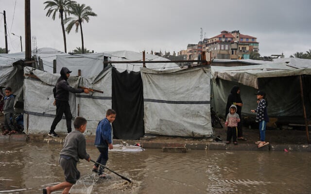 Displaced Palestinian children walk through a rain-soaked tent camp following heavy rainfall in Deir al-Balah, central Gaza Strip, Thursday, March, 26, 2026. (AP/Abdel Kareem Hana) Displaced Palestinian children walk through a rain-soaked tent camp following heavy rainfall in Deir al-Balah, central Gaza Strip, Thursday, March, 26, 2026. (AP/Abdel Kareem Hana)