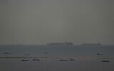 Fishing boats dot the sea as cargo ships, in the background, sail through the Arabian Gulf toward the Strait of Hormuz off the United Arab Emirates, March 27, 2026. (AP Photo)
